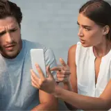 Coppia sconvolta guarda il telefono, affrontando il difficile percorso su come superare un tradimento.