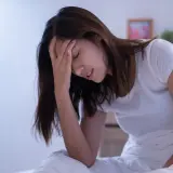 Donna a letto con la mano sulla fronte, visibilmente sofferente. L'insonnia pre ciclo le impedisce di dormire.