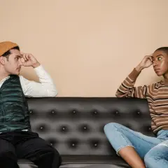 Coppia pensierosa sul divano, forse riflettono sui sintomi della sindrome di Peter Pan, evitando il contatto visivo.