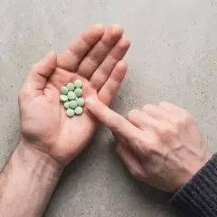 Mano aperta con un mucchietto di pillole verdi, come un trittico gocce. Un dito le indica.