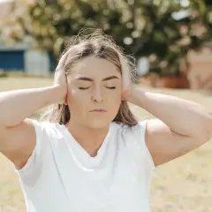 Ragazza con le orecchie tappate, occhi chiusi, espressione di ansia. Il rumore del mondo esterno è troppo forte.