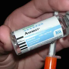 Mano che tiene una fiala di Anesket (ketamina) con siringa, suggerendo potenziali ketamina effetti positivi in contesti medici.