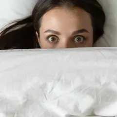 Occhi spalancati sotto le coperte, un'espressione di pura paura di dormire.