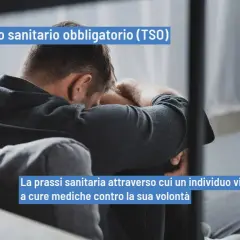 Uomo seduto con la testa tra le braccia, simbolo di sofferenza. Il TSO, trattamento sanitario obbligatorio, è una prassi medica imposta.