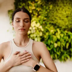 Donna con gli occhi chiusi e le mani sul petto, pratica la respirazione diaframmatica davanti a una parete verde.