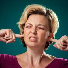 Donna di trent'anni si tappa le orecchie, con espressione infastidita.