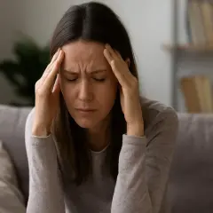 Donna con le mani sulle tempie, occhi chiusi, espressione di profondo stress e possibile esaurimento nervoso.