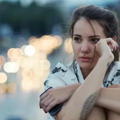 Giovane donna pensierosa, con luci sfocate sullo sfondo, sembra voler rimuovere ricordi traumatici.
