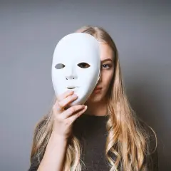 Ragazza bionda con maschera bianca, un'espressione che evoca il disturbo istrionico di personalità.