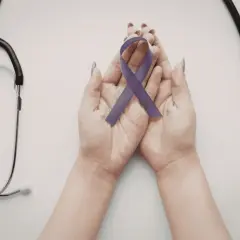 Mani che sorreggono un nastro viola, simbolo di consapevolezza sulla fibromialgia e i suoi sintomi iniziali, con uno stetoscopio a lato.