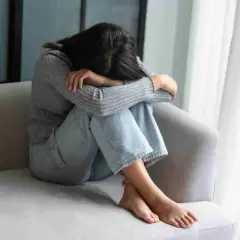 Ragazza rannicchiata sul divano, con la testa tra le ginocchia, soffre di fobia del vomito.