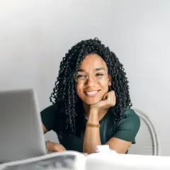 Donna sorridente con occhiali, laptop e libri. Si chiede dopo quante sedute di psicoterapia si vedono i risultati.