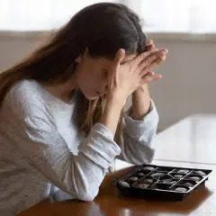 Donna con le mani sul viso, davanti a una scatola di cioccolatini, forse cercando un antidepressivo naturale più potente.