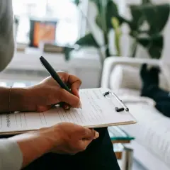 Mani che scrivono su un blocco note, mentre una persona è sdraiata su un divano. Un momento di riflessione per capire se per l'ansia meglio psicologo o psichiatra.