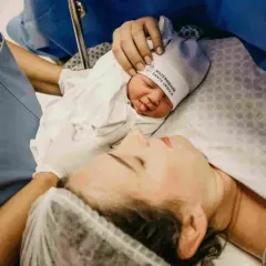 Mommy and baby bonding after cesareo. A nurse's hand gently holds the newborn's hat.