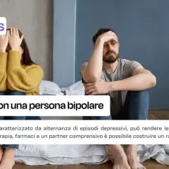 Coppia seduta a letto, uno copre il viso, l'altro con la mano sulla fronte. Immagine su come comportarsi con una persona bipolare.