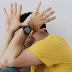 Uomo con le mani alzate a protezione del viso, forse per la paura delle cimici. Indossa una maglietta gialla e un orologio.