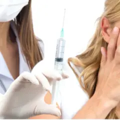 Una donna con espressione di paura degli aghi, copre il viso mentre un'infermiera con guanti bianchi tiene una siringa.
