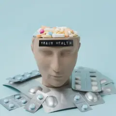Testa di manichino piena di pillole, con la scritta "BRAIN HEALTH". Intorno, blister di psicofarmaci, suggerendo che il neurologo può prescrivere psicofarmaci.