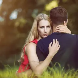 Una donna bionda abbraccia un uomo, il suo sguardo intenso interroga sul perchè l'uomo tradisce.