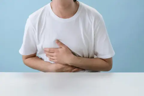 Persona con le mani sull'addome, che esprime disagio. Potrebbe soffrire di diarrea da stress.