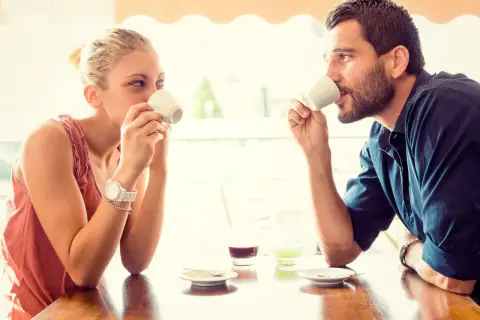 Coppia al bar, lui la guarda intensamente, un uomo innamorato in segreto che cerca il suo sguardo mentre bevono un caffè.