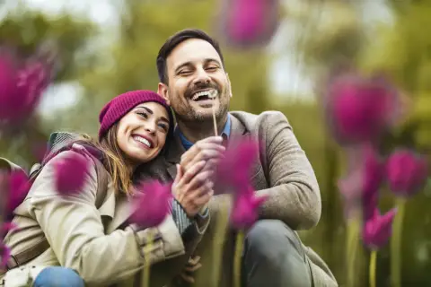 Coppia felice che ride tra i fiori. Un abbraccio sincero, un sorriso contagioso: ecco 15 segnali di una relazione sana.