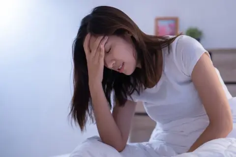 Donna a letto con la mano sulla fronte, visibilmente sofferente. L'insonnia pre ciclo le impedisce di dormire.