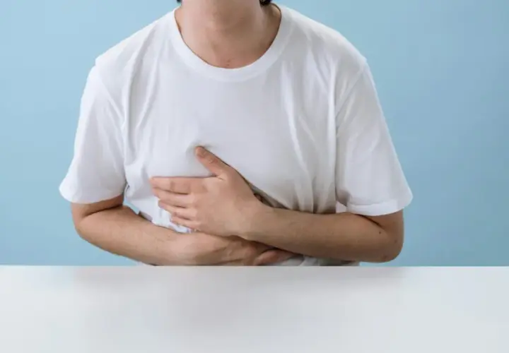 Persona con le mani sull'addome, che esprime disagio. Potrebbe soffrire di diarrea da stress.