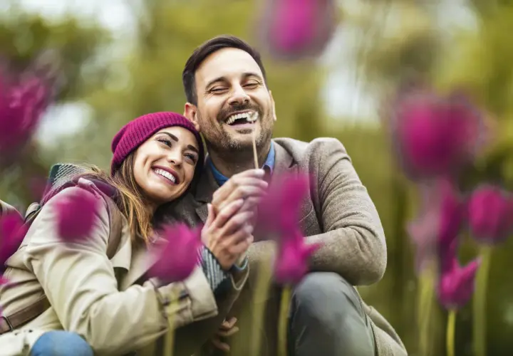 Coppia felice che ride tra i fiori. Un abbraccio sincero, un sorriso contagioso: ecco 15 segnali di una relazione sana.