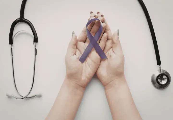 Mani che sorreggono un nastro viola, simbolo di consapevolezza sulla fibromialgia e i suoi sintomi iniziali, con uno stetoscopio a lato.