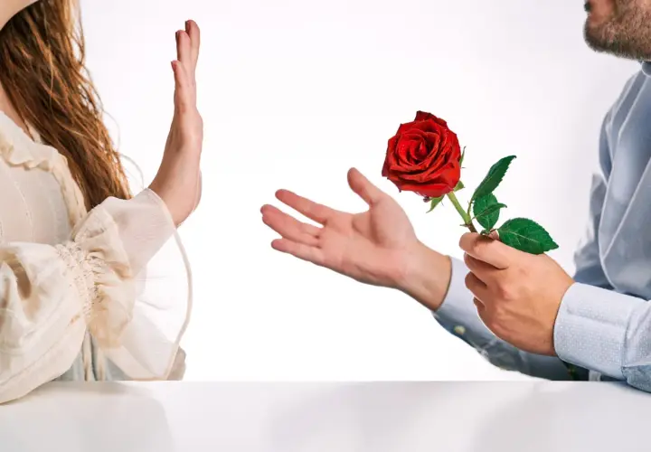 Una mano respinge una rosa rossa offerta da un uomo. Un'immagine che evoca il tema di come superare un rifiuto in amore.