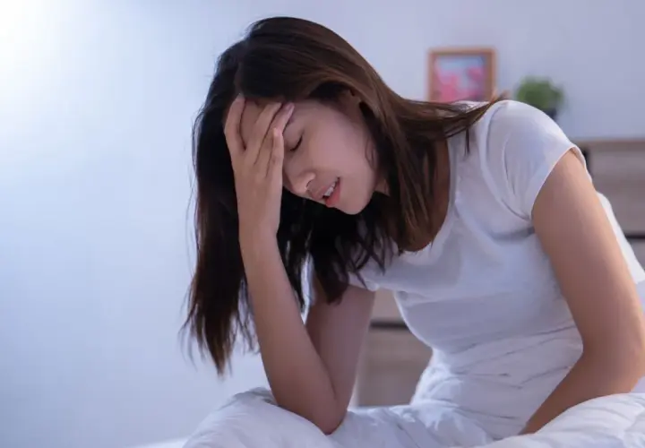 Donna a letto con la mano sulla fronte, visibilmente sofferente. L'insonnia pre ciclo le impedisce di dormire.