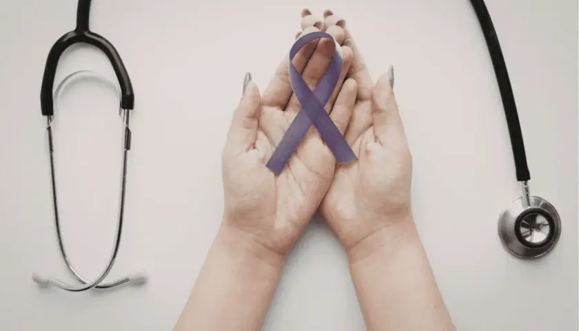 Mani che sorreggono un nastro viola, simbolo di consapevolezza sulla fibromialgia e i suoi sintomi iniziali, con uno stetoscopio a lato.