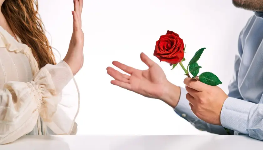 Una mano respinge una rosa rossa offerta da un uomo. Un'immagine che evoca il tema di come superare un rifiuto in amore.