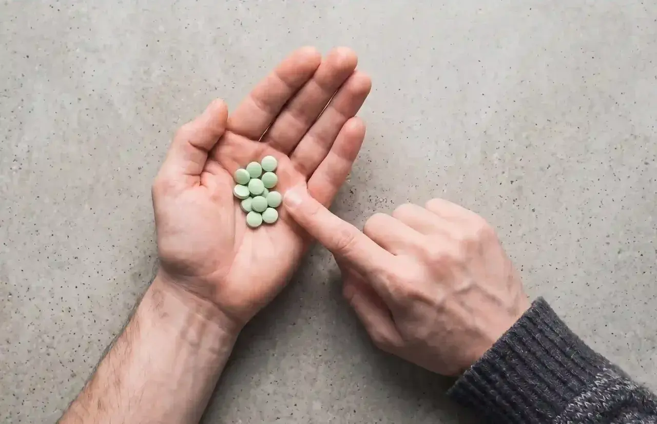 Mano aperta con un mucchietto di pillole verdi, come un trittico gocce. Un dito le indica.