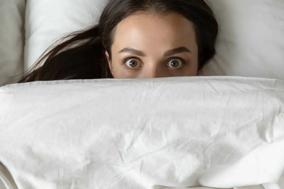 Occhi spalancati sotto le coperte, un'espressione di pura paura di dormire.