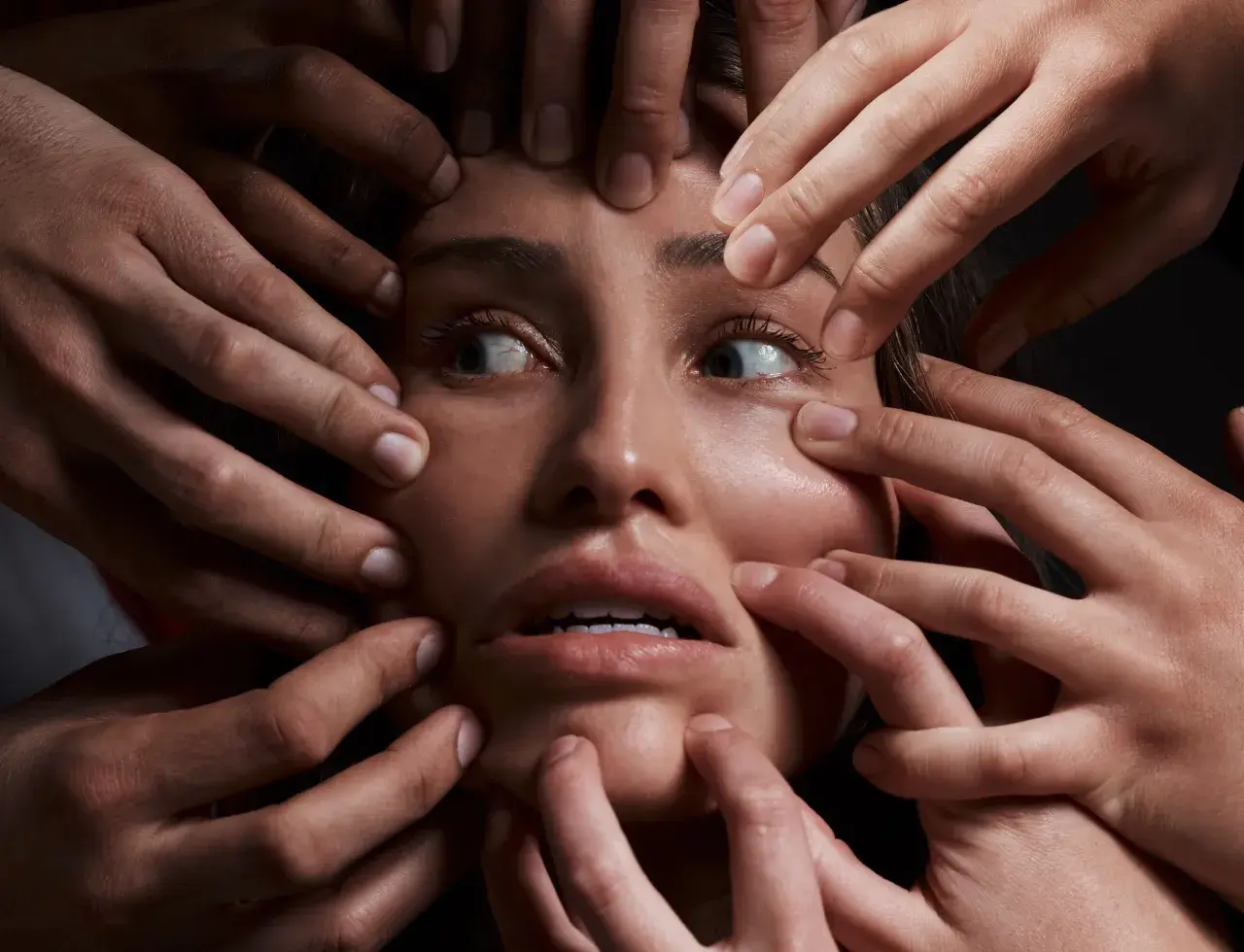 Volto di donna circondato da mani che la stringono, espressione di disagio, forse un simbolo del disturbo schizoide di personalità.