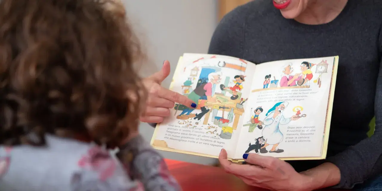 Donna legge un libro illustrato a un bambino, un momento di apprendimento che supporta il rinnovo certificazione DSA.