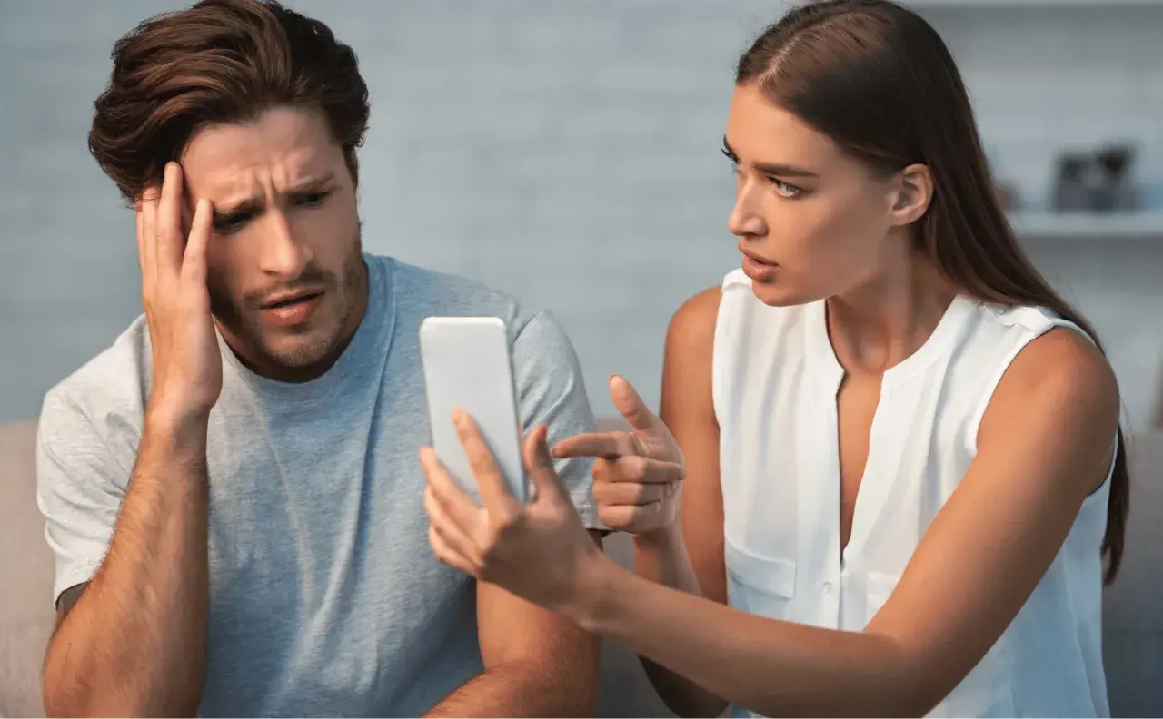 Coppia sconvolta guarda il telefono, affrontando il difficile percorso su come superare un tradimento.