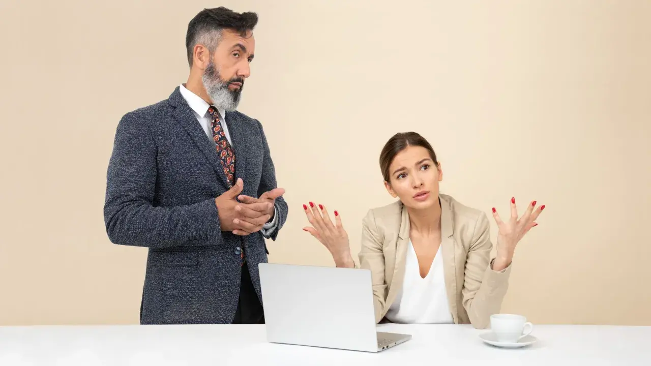 Un collega che vuole comandare, con un'espressione autoritaria, parla con una collega che sembra confusa e frustrata.