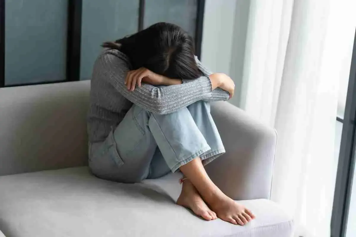 Ragazza rannicchiata sul divano, con la testa tra le ginocchia, soffre di fobia del vomito.