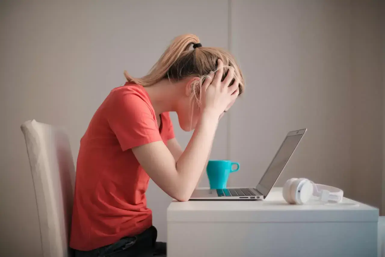 Donna con le mani tra i capelli, frustrata davanti al laptop. La cistite è rabbia repressa, un peso che schiaccia.