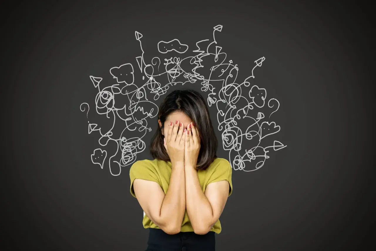 Donna con le mani sul viso, circondata da disegni caotici. Un'immagine che evoca la difficoltà nel come trattare un paranoico, con pensieri confusi e ansia.