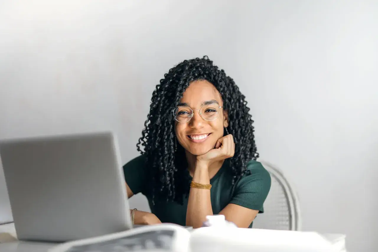 Donna sorridente con occhiali, laptop e libri. Si chiede dopo quante sedute di psicoterapia si vedono i risultati.