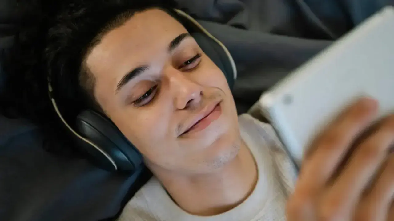 Giovane con cuffie e tablet, forse in un momento di solitudine, tra autoerotismo e depressione.