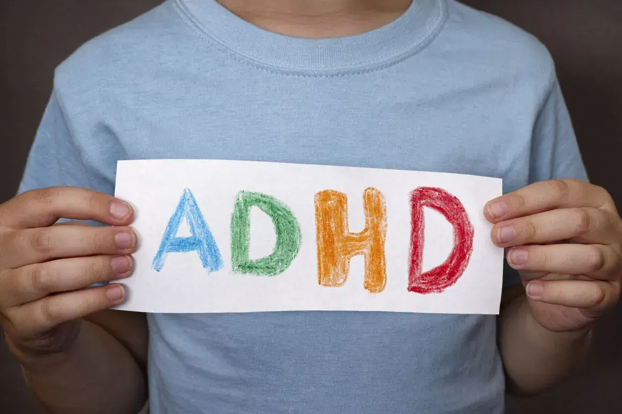 Bambino tiene un foglio con la scritta ADHD colorata, che rappresenta i sintomi di questa condizione.