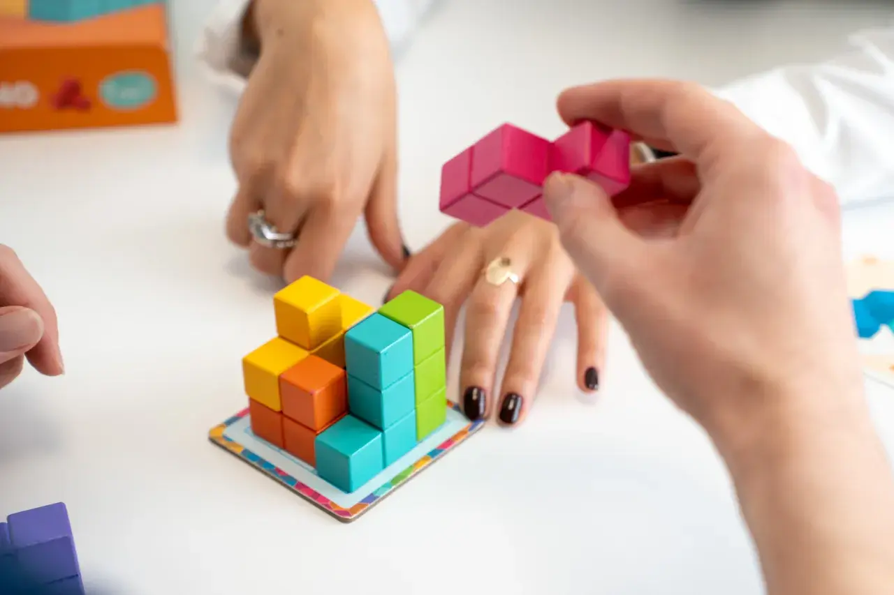 Mani che assemblano blocchi colorati, un gioco che stimola l'alto potenziale cognitivo.