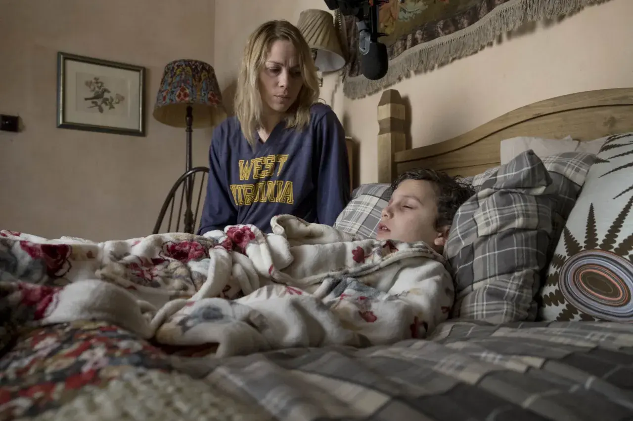 Donna preoccupata veglia un bambino che sembra soffrire di paralisi del sonno, immobile nel letto.