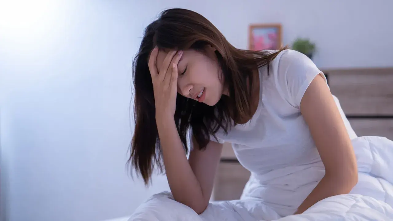Donna a letto con la mano sulla fronte, visibilmente sofferente. L'insonnia pre ciclo le impedisce di dormire.